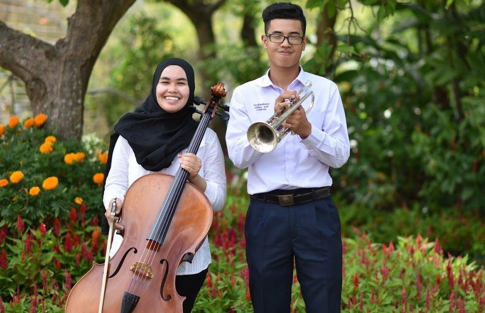 Awatif and Kasidach stand side by side with their instruments in a garden, smiling