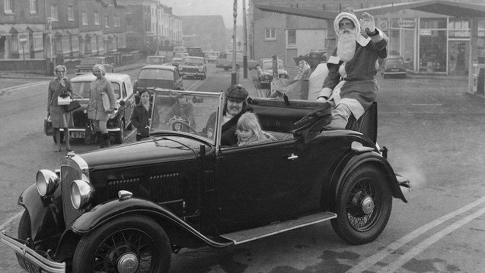 Santa Claus sitting on the back of a car