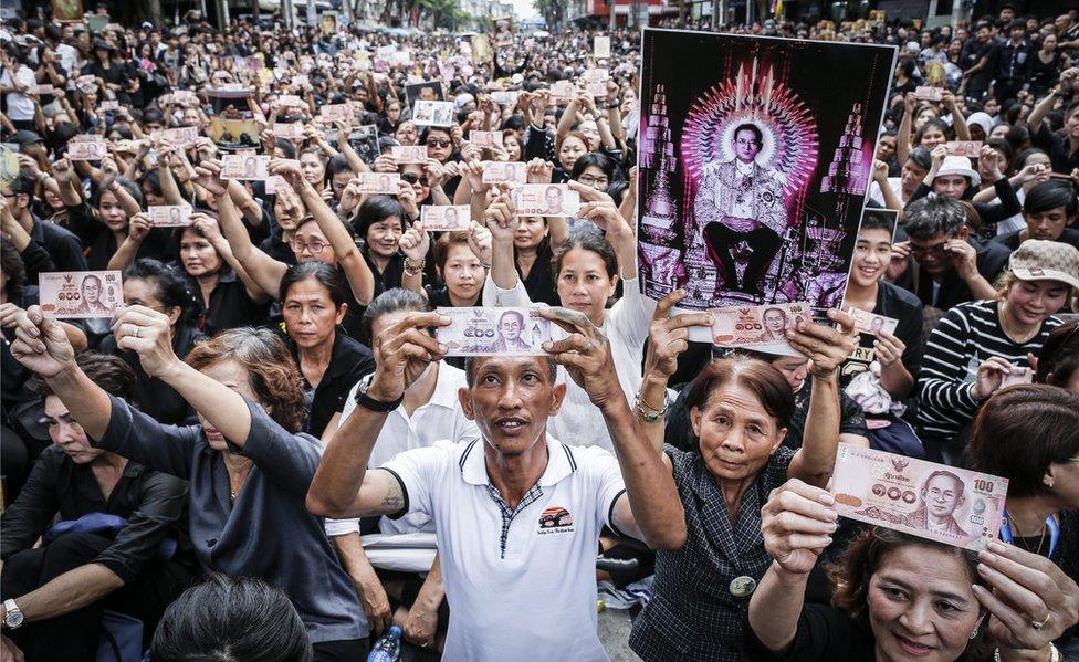 In this picture, Thai well-wishers hold Thai Baht banknotes with pictures of the King Bhumibol Adulyadej as they wait for the procession to move his body