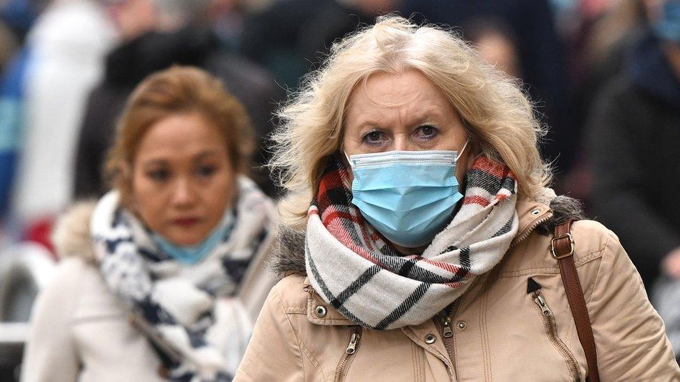 A woman in a mask walks down a street in Cardiff, Wales