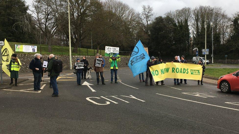 Extinction Rebellion protesters holding up 'No New Roads' banner and blocking the roundabout near Norfolk County Hall