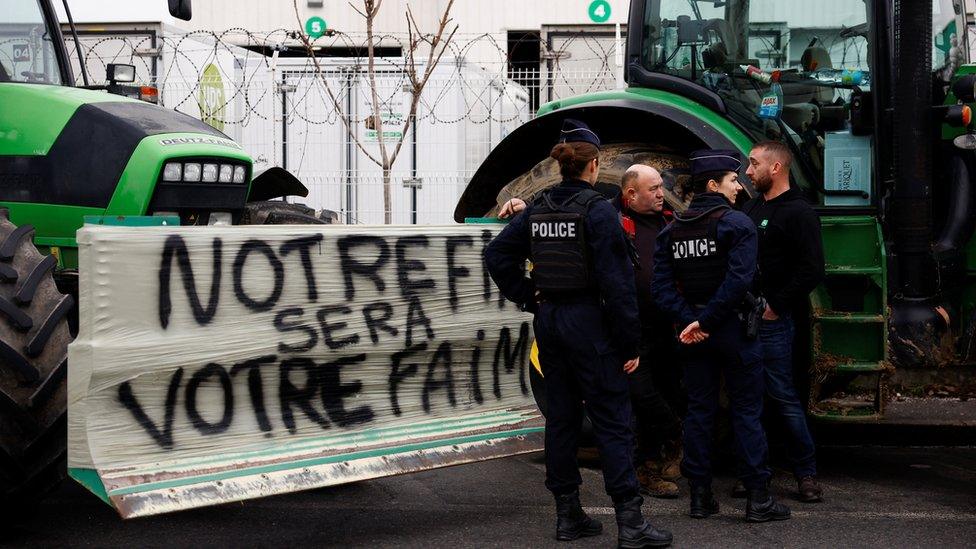 Police officers speak with demonstrators as tractors are parked in front of Rungis food market