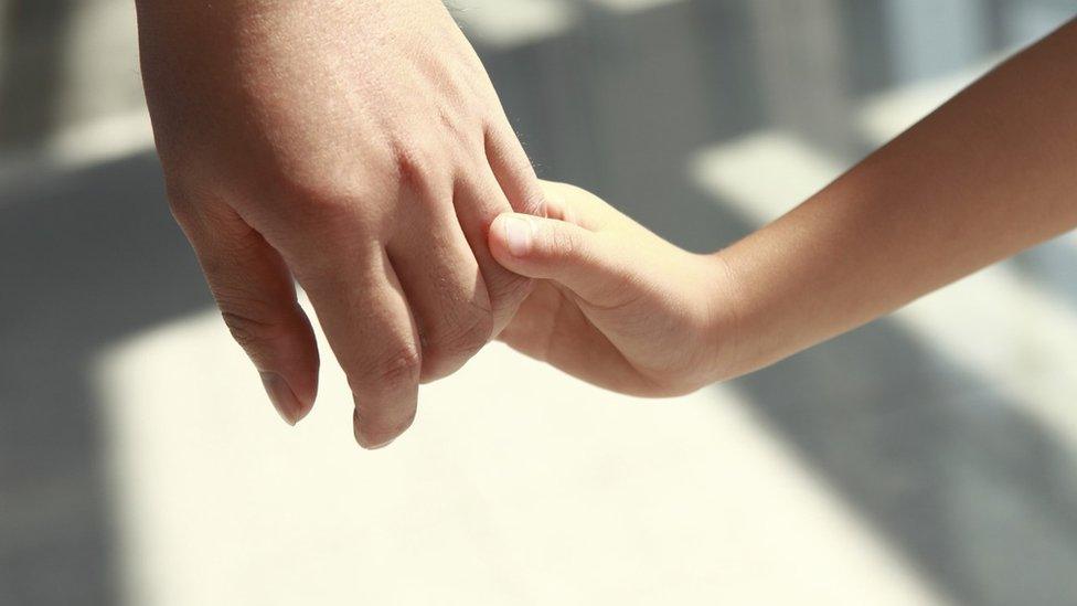 Child holding hands with an adult