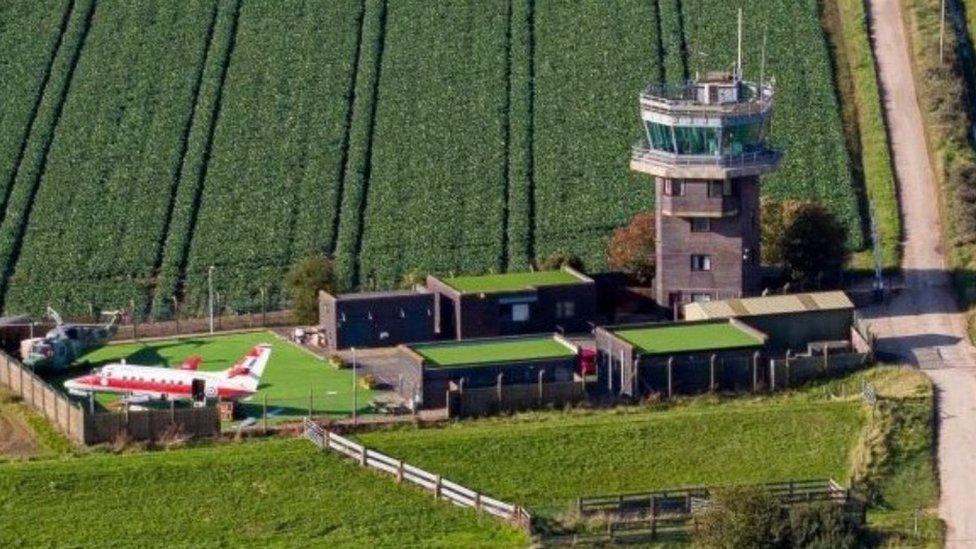 Aerial view of former airfield control tower with a helicopter and aircraft next to it