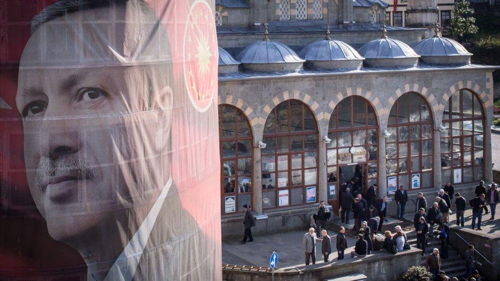 Men exit a mosque after afternoon prayer behind a banner showing the portrait of Turkish President Recep Tayyip Erdogan hanging from a building on 10 April 2017 in Rize, Turkey.