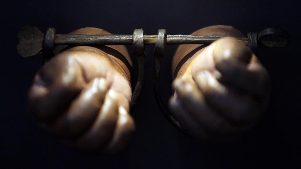 Two hands bound in wooden shackles