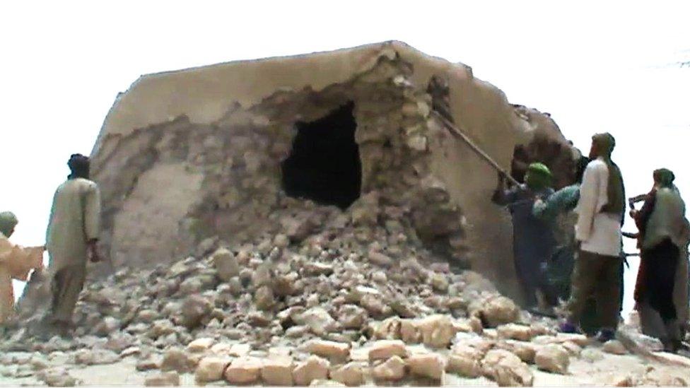 Men pulling down a mausoleum with metal sticks, 2012