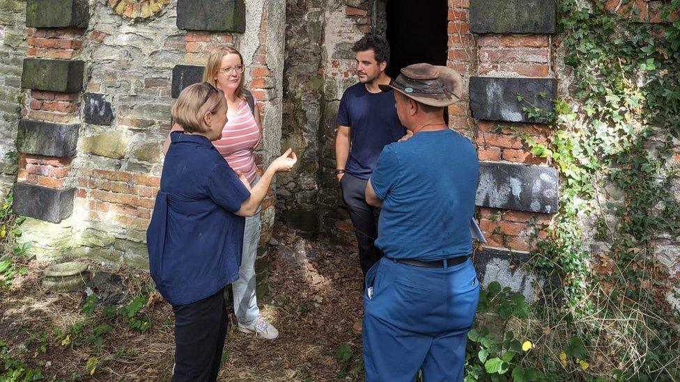 Four people speaking in front of an old wall in the wood