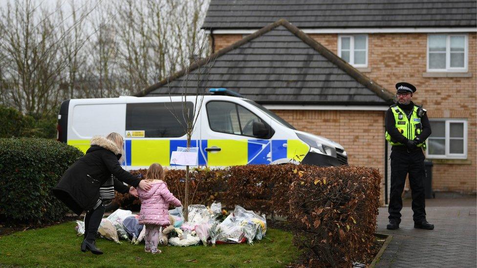 A woman and girl lay flowers, watched by a police officer