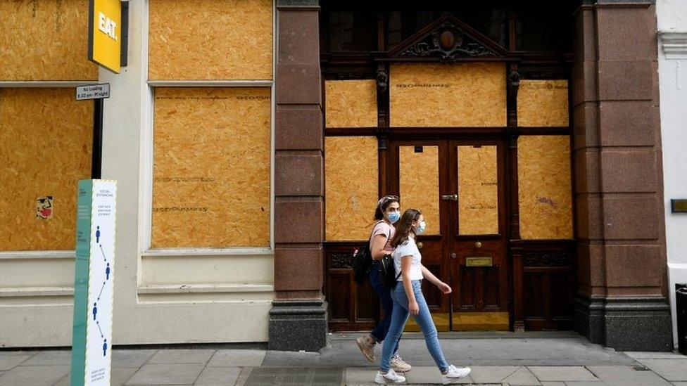 Women walking past boarded up London cafe