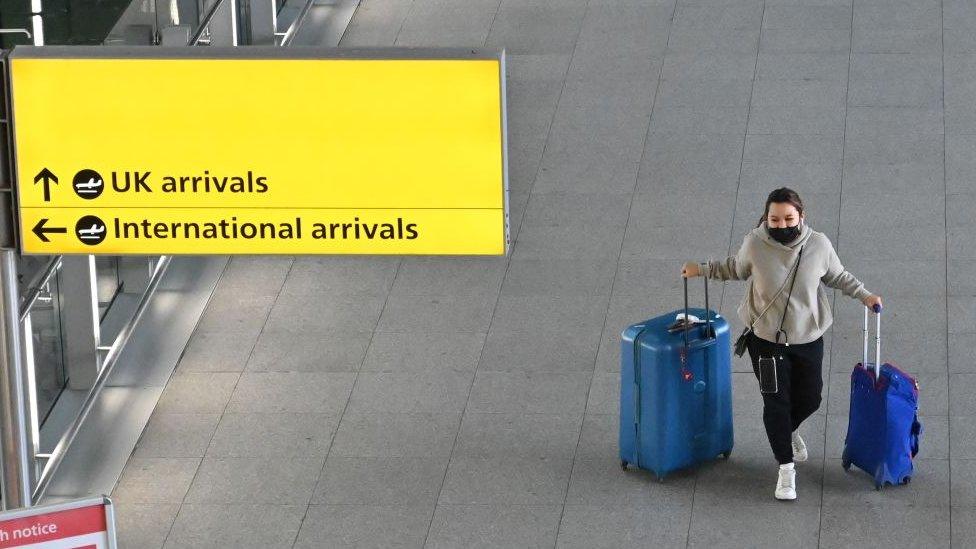 Woman travels through Heathrow airport with two suitcases and wearing a coronavirus mask