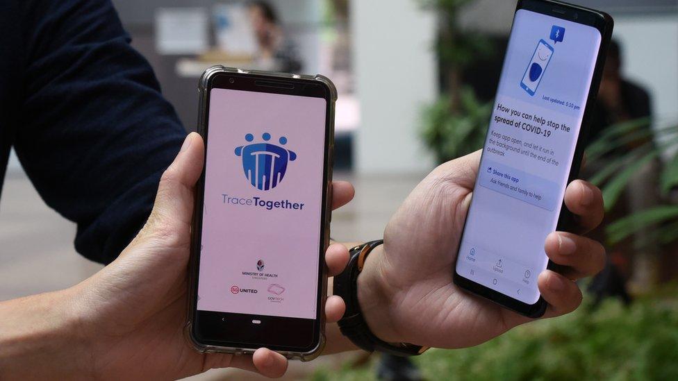 Two people hold up phones running the TraceTogether app in Singapore