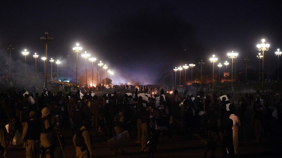 Pakistani police officers stand next to supporters of executed Islamist Mumtaz Qadri, gathered next to a burning trailer truck