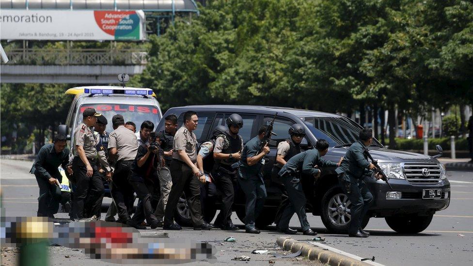 Dead bodies are seen as Indonesian police hold rifles while walking behind a car for protection in Jakarta January 14, 2016