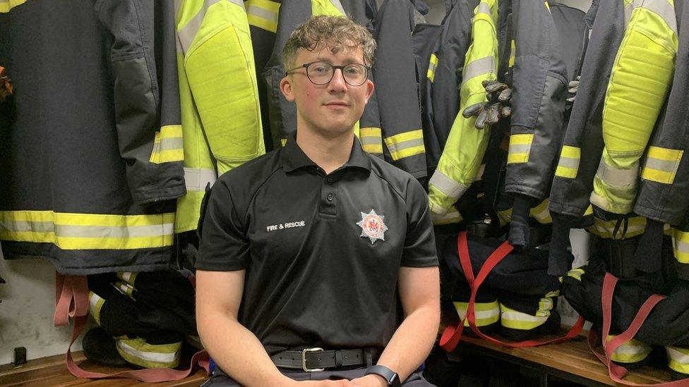 Anthony Seaward sitting in front of firefighter uniforms