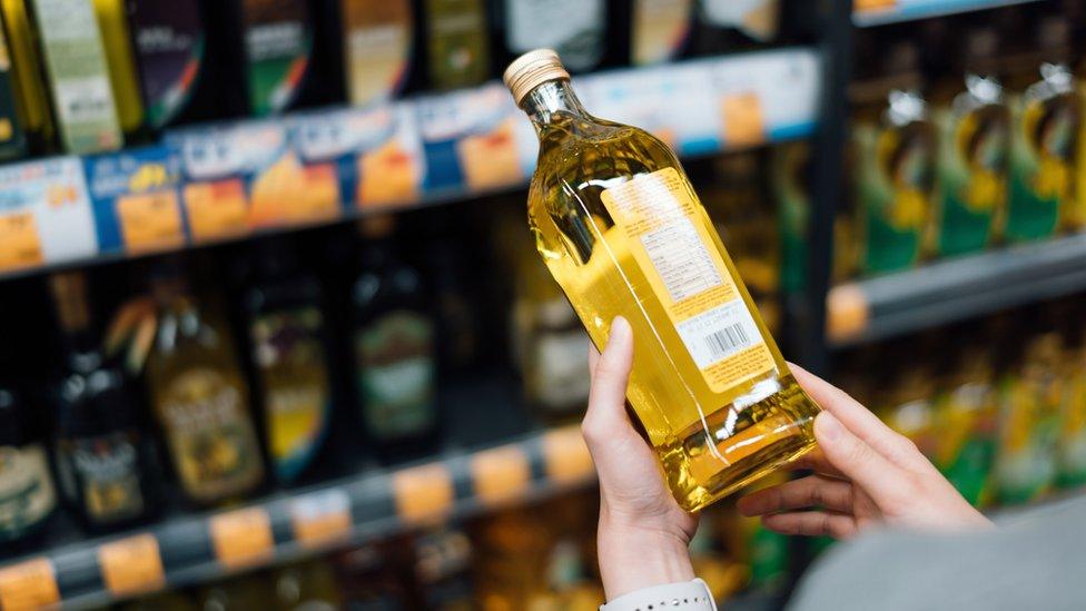 Woman grocery shopping in a supermarket holding a bottle of sunflower oil