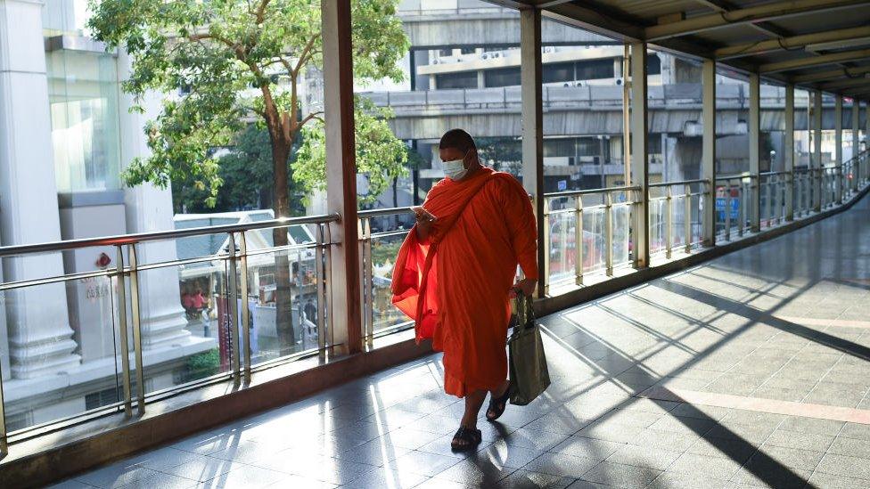 A monk wearing protective face mask walks a past skywalk amid a new wave of Covid-19 infections in Bangkok,