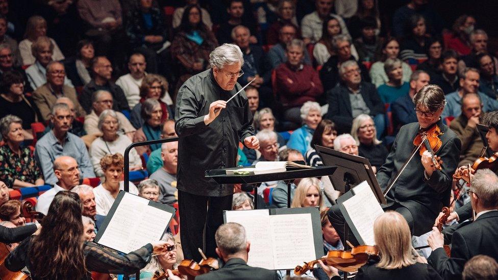 A conductor stands in the centre of musicians from the London Symphony Orchestra at the Bristol Beacon