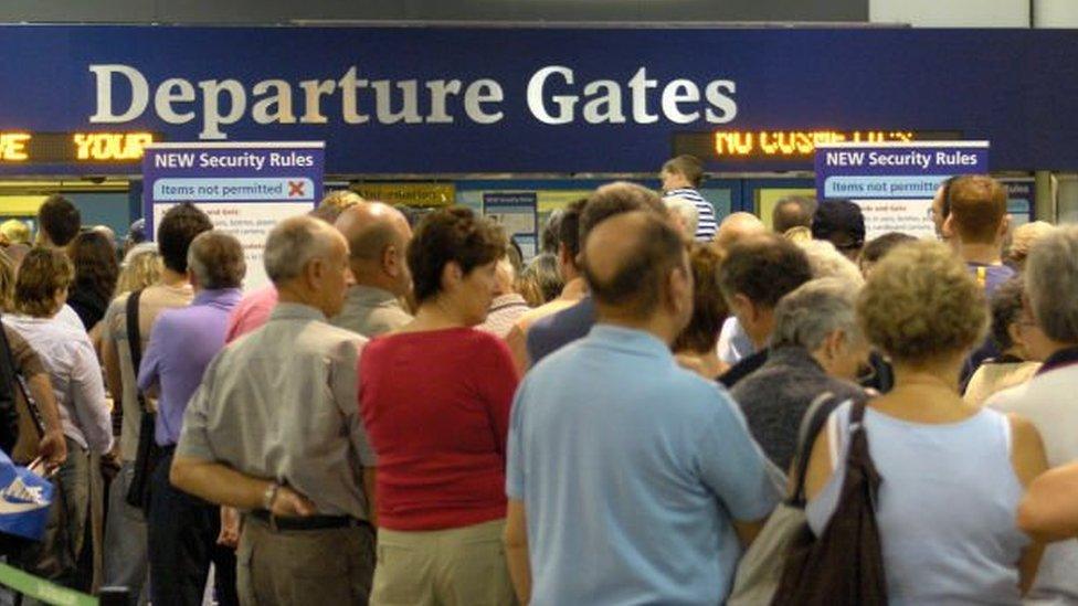 Passengers standing by an airport departure gate sign