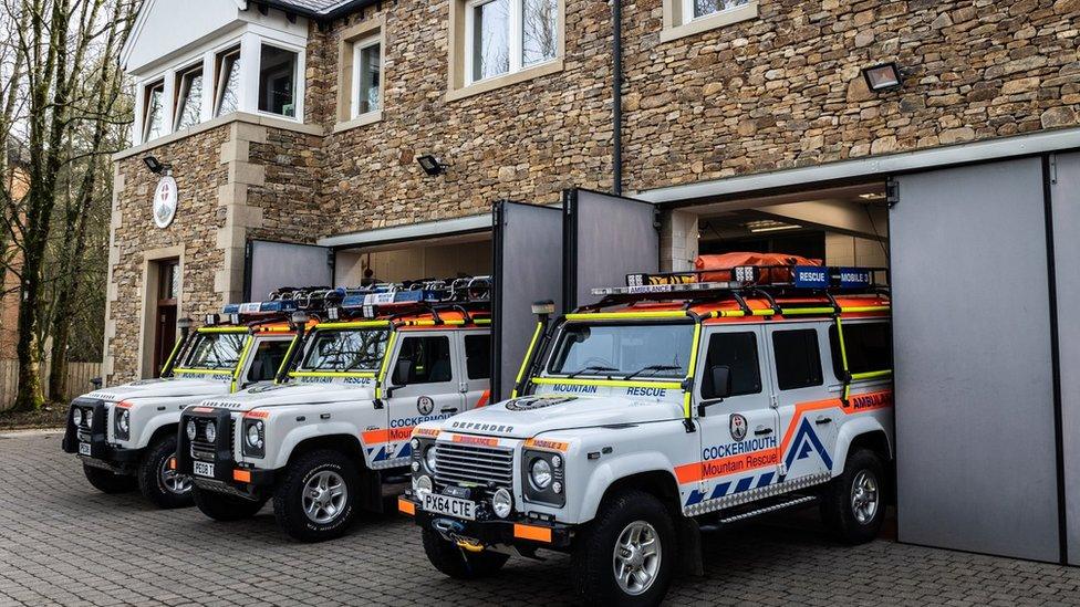 Three mountain rescue Land Rovers lined up outside a smart stone building