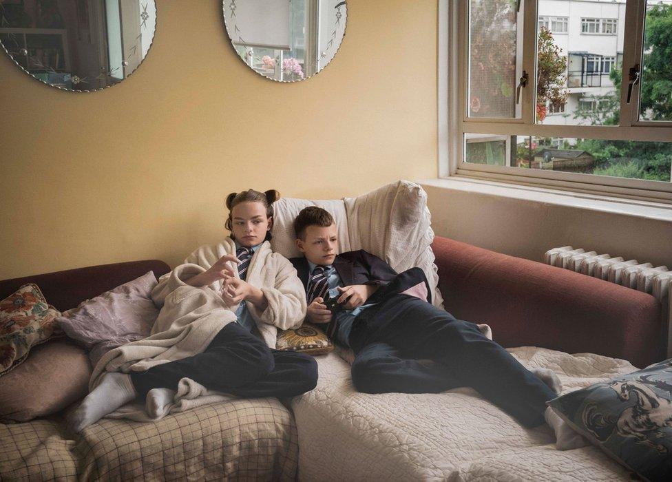 Two school children lying on a sofa looking at a television