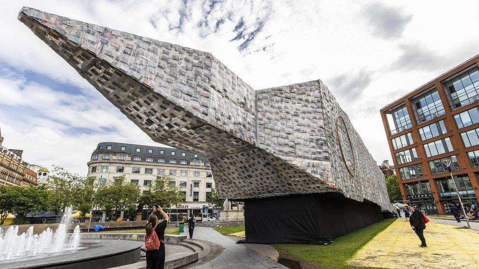 Members of the public look at an art installation called Ben Ben Lying Down with Political Books by Marta Minujin