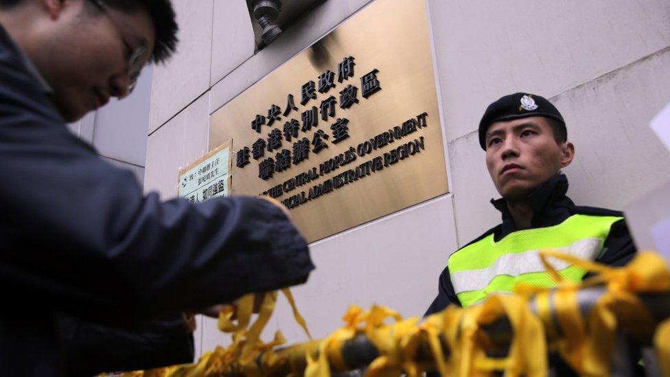 A man ties a yellow ribbon onto a barricade outside the residence of Beijing's representative in Hong Kong