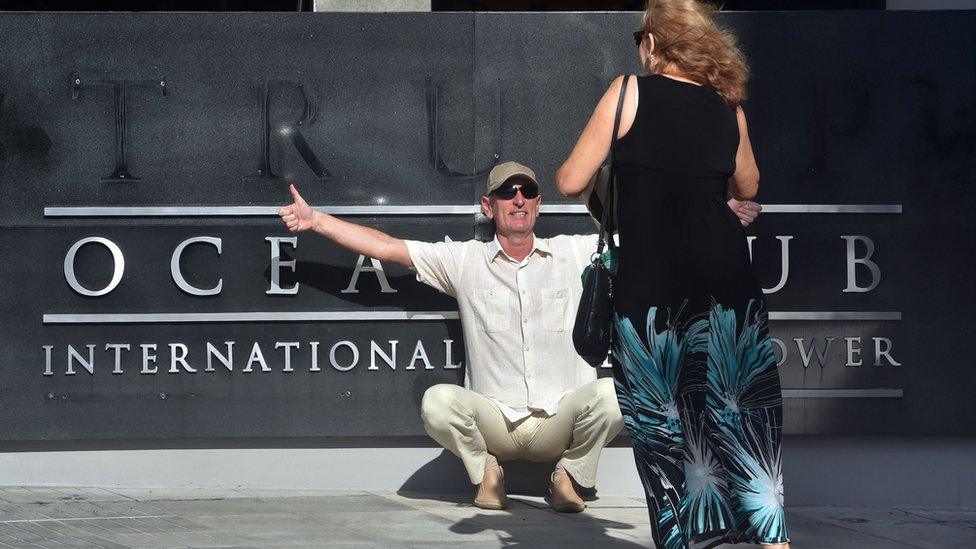 A tourist poses for pictures after the Trump logo was removed from the entrance to the Trump Ocean Club International Hotel and Tower luxury complex in Panama City on March 5, 2018.