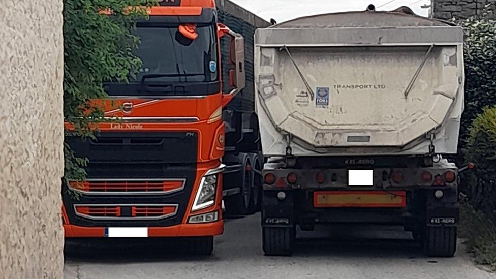 An orange lorry and a white lorry passing each other in a narrow lane