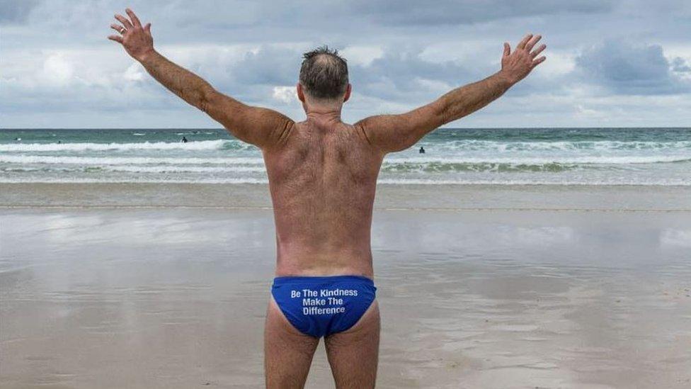 Speedo Mick on a beach with arms in the air