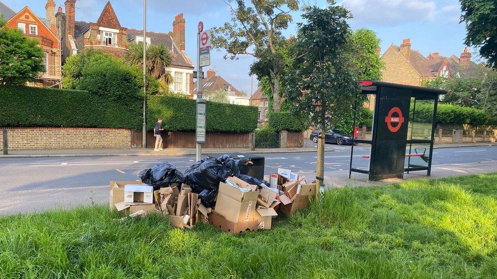 Dozens of broken down boxes and multiple black sacks are piled up behind a bus stop pole on the edge of Wandsworth Common