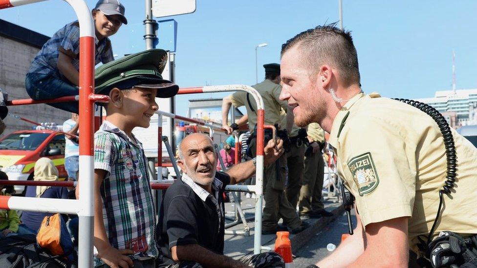 German police officer and a migrant boy joke with the officer"s cap while migrants wait for a bus after their arrival at the main train station in Munich, southern Germany, September 1, 2015.