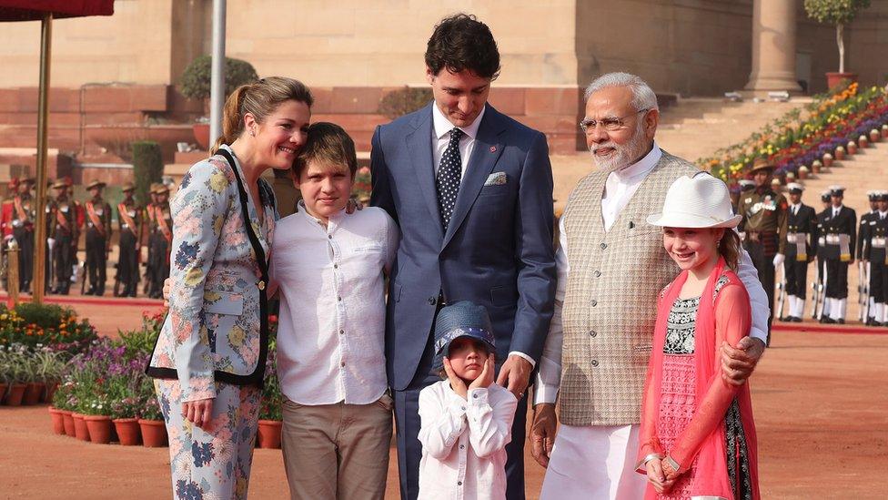 Hadrien Trudeau pulling his hat over his face in a photo with Narendra Modi