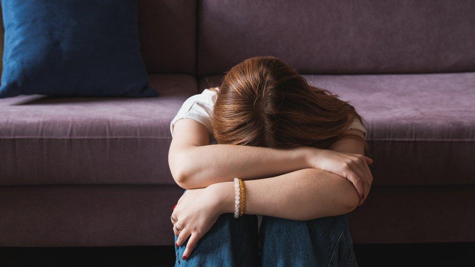 A woman with her head in her hands leaning against a sofa