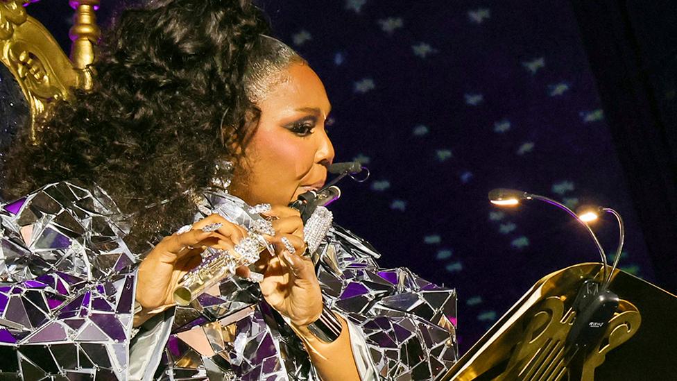 Lizzo and Sir James Galway (out of shot) sit on gold thrones as they perform a flute duet at the Met Gala