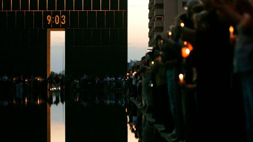 A 09:03 archway and pool lined with people remembering the attack, with candles