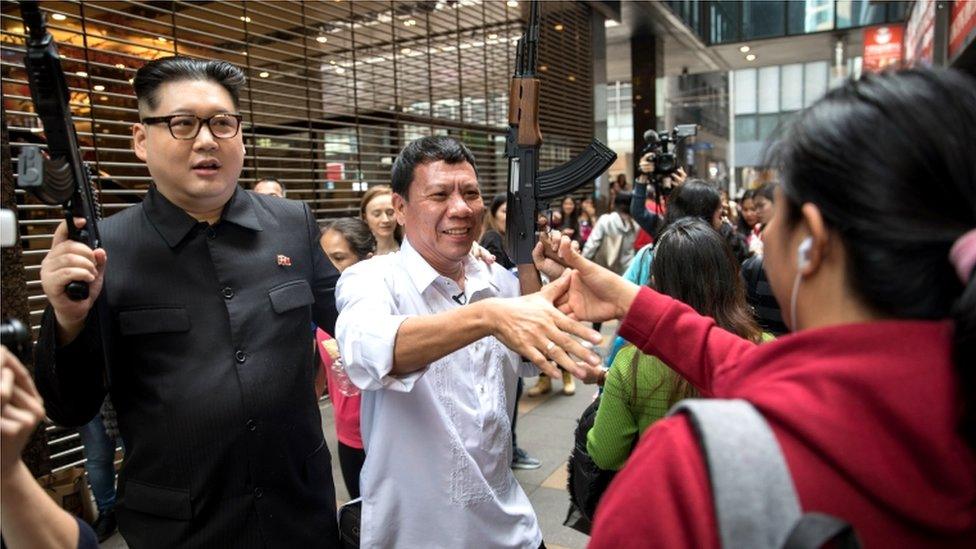 Howard X (L) and Cresencio Extreme are greeted by Filipino maids outside a Jollibee fried chicken restaurant in Hong Kong