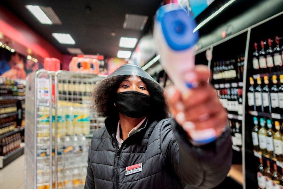 A liquor store worker measures temperatures of customers at the entrance of a shop in Melville, Johannesburg, on August 18, 2020. - South Africa moved into level two of a five-tier lockdown on August 18, 2020, to continue efforts to curb the spread of the COVID-19 coronavirus. Under level two liquor and tobacco sales will resume.