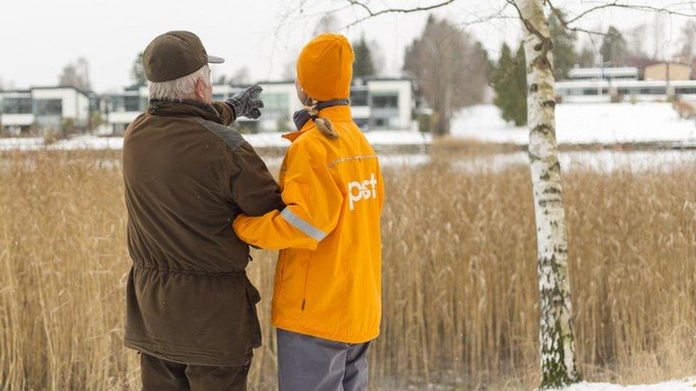 A promotional photo from Posti showing a female worker linking arms with an elderly man outside in the snow