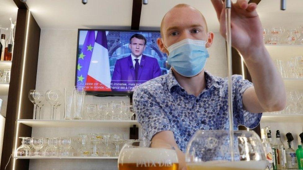 A man pours a beer in a bar while President Macron is on the TV behind him.