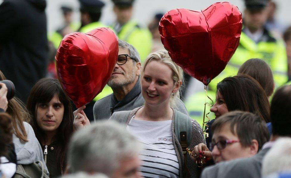 A woman holds up two heart-shaped balloons at a vigil in London