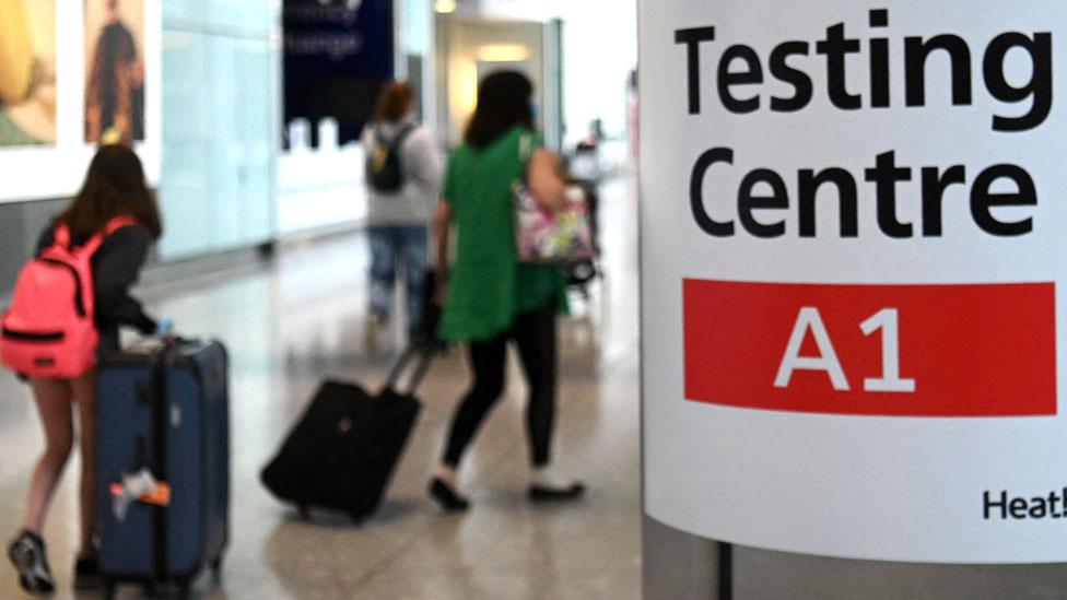 Passengers push their luggage past signage displaying the way to a Covid-19 test centre, in Terminal 5 at Heathrow airport in London, in June 2021