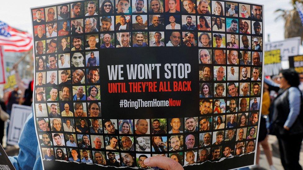 An image showing a demonstrator holding a poster with photos of the hostages during a rally calling for their release