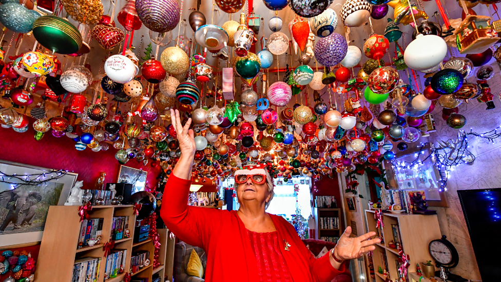 Nanna Baubles standing underneath hundreds of Christmas baubles hanging from her living room ceiling