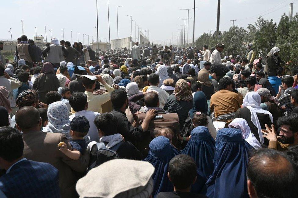 Afghans gather on a roadside near the military part of the airport in Kabul on August 20, 2021, hoping to flee from the country after the Taliban's military takeover