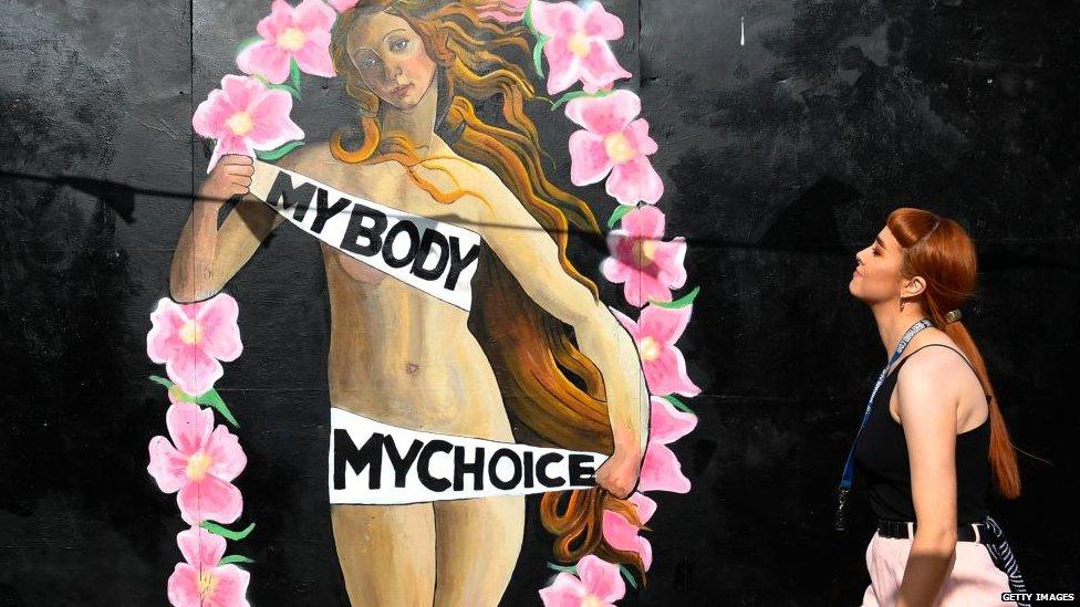 A woman walks in front of a pro-choice mural