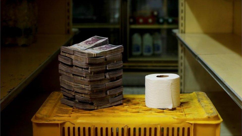 A pile of bolivar notes is stacked up next to a toilet roll