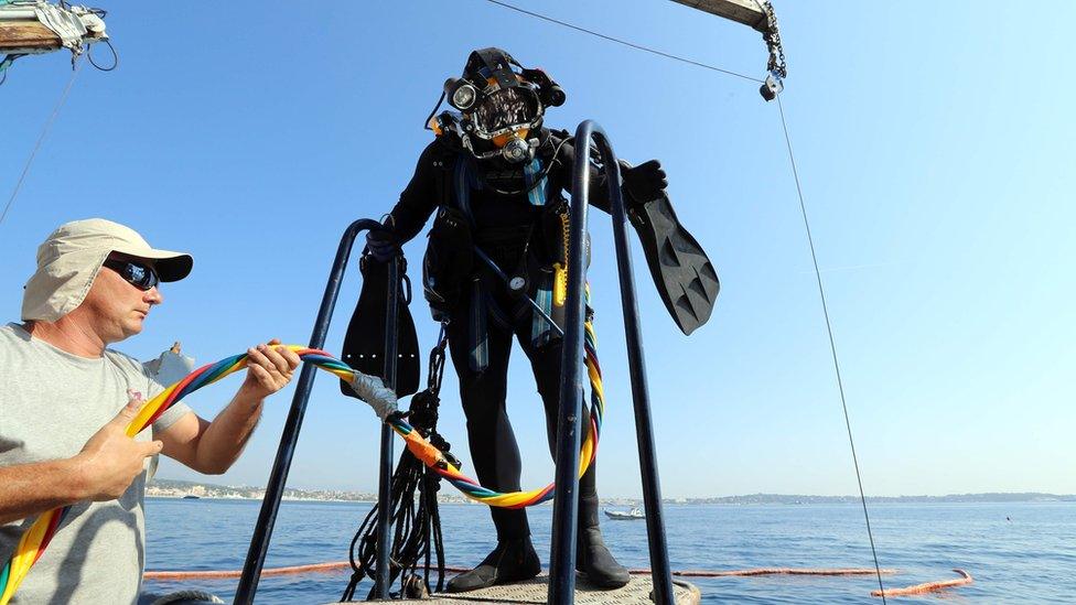 A diver in full gear, about to enter the sea from a boat