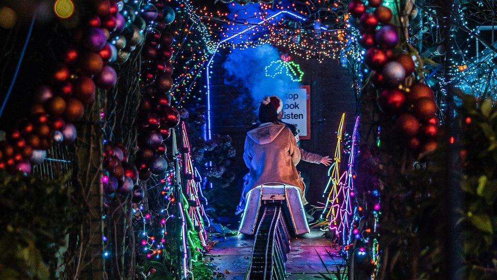 Person riding miniature train under Christmas lights