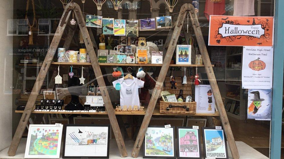 An image of the storefront of Eclectic gift shop. there are small pumpkins, posters and figurines in the window.